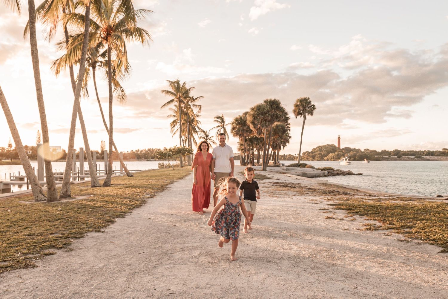 A scenic beach pathway lined with palm trees at sunset while people stroll along the sandy shoreline.