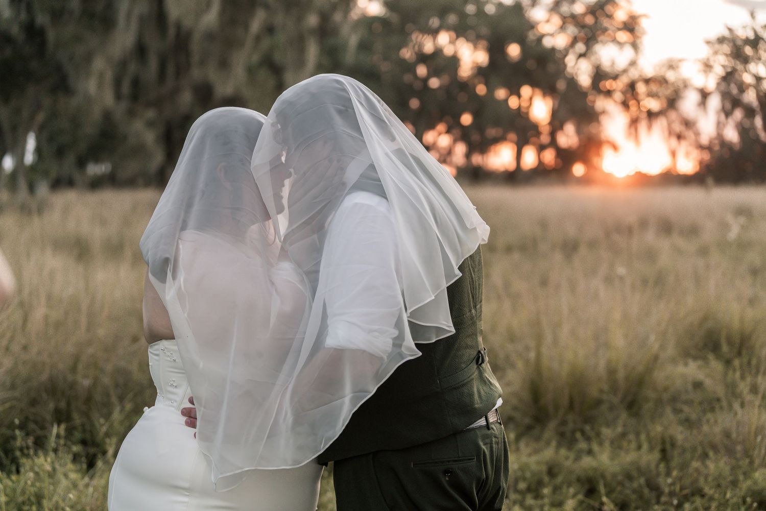 A romantic sunset silhouette of a couple embracing in a field with a veil flowing in the golden light.