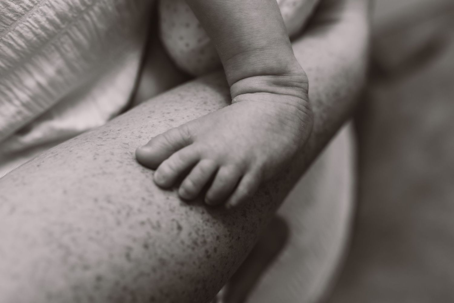 Close-up black and white photo of a newborn baby's tiny feet and toes resting on an adult's arm.