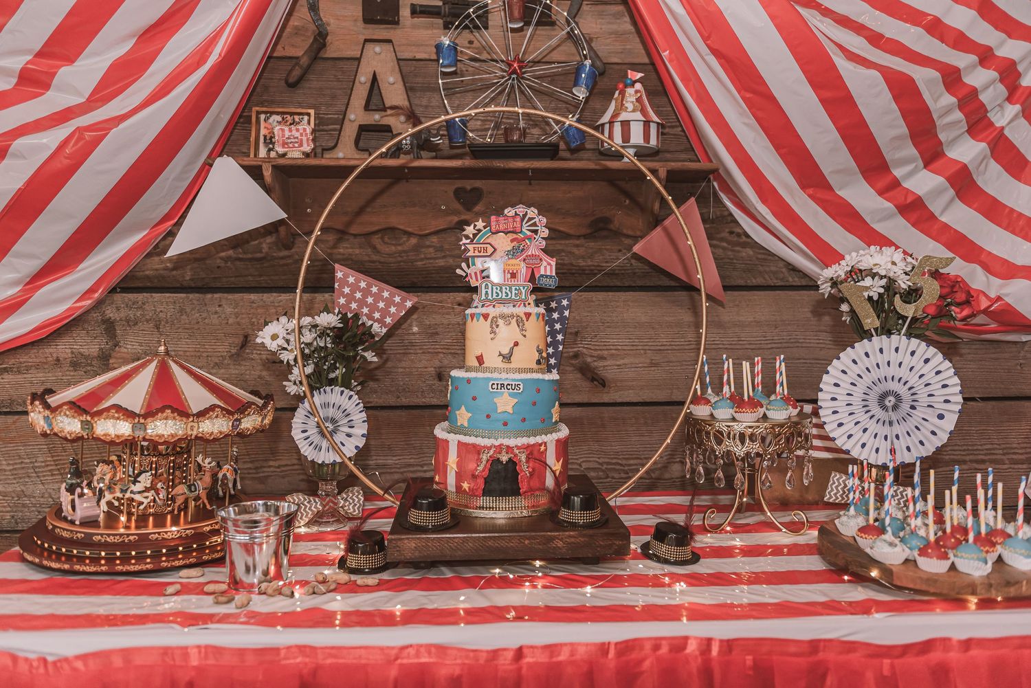 A vintage circus-themed dessert table with red striped tent decor and a multi-tiered cake centerpiece on a wooden backdrop.