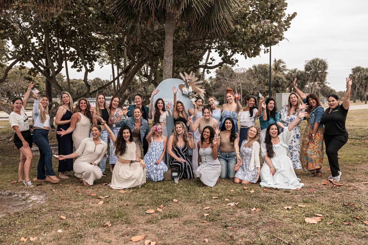Large group in coordinated blue and white attire gathered outdoors under palm trees for a casual photo.