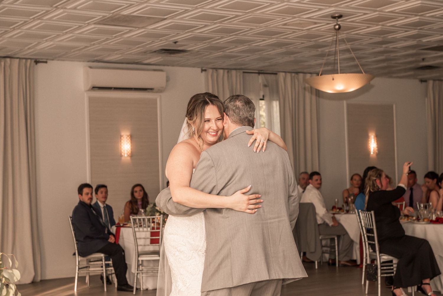 Emotional dance moment at wedding reception with guests seated at tables in elegant banquet hall.