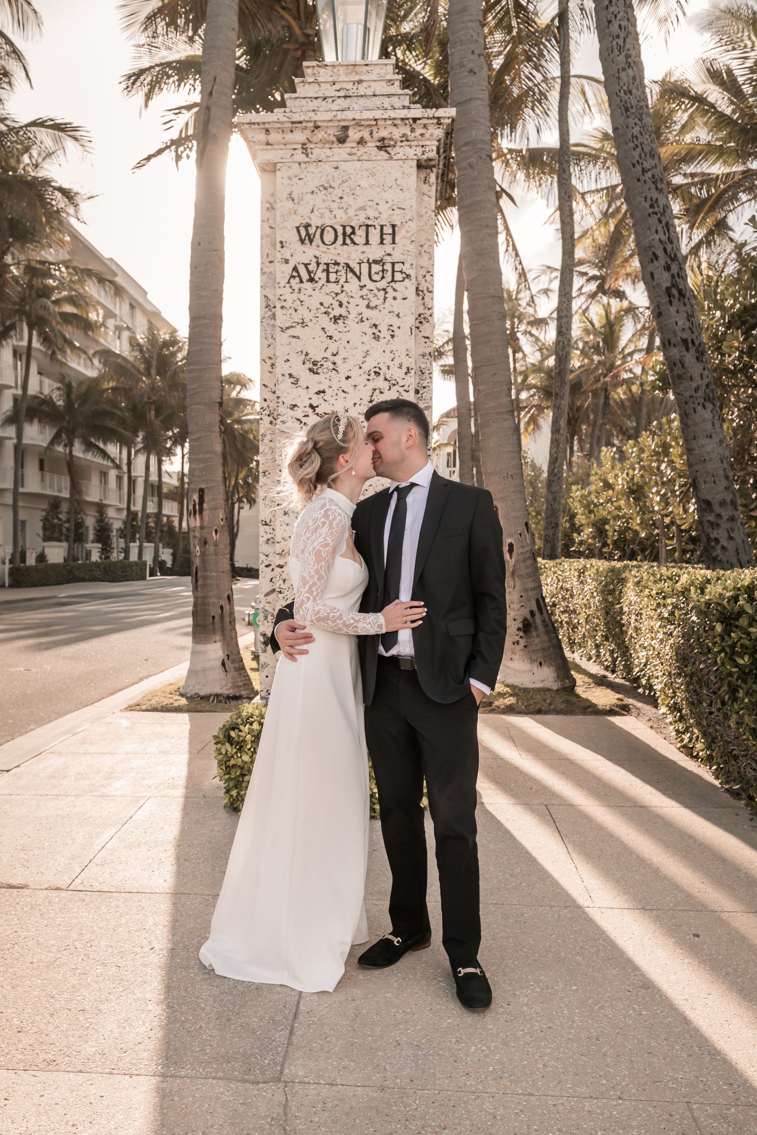 Bride and groom kissing in front of Worth Avenue sign surrounded by palm trees in Palm Beach, FL.