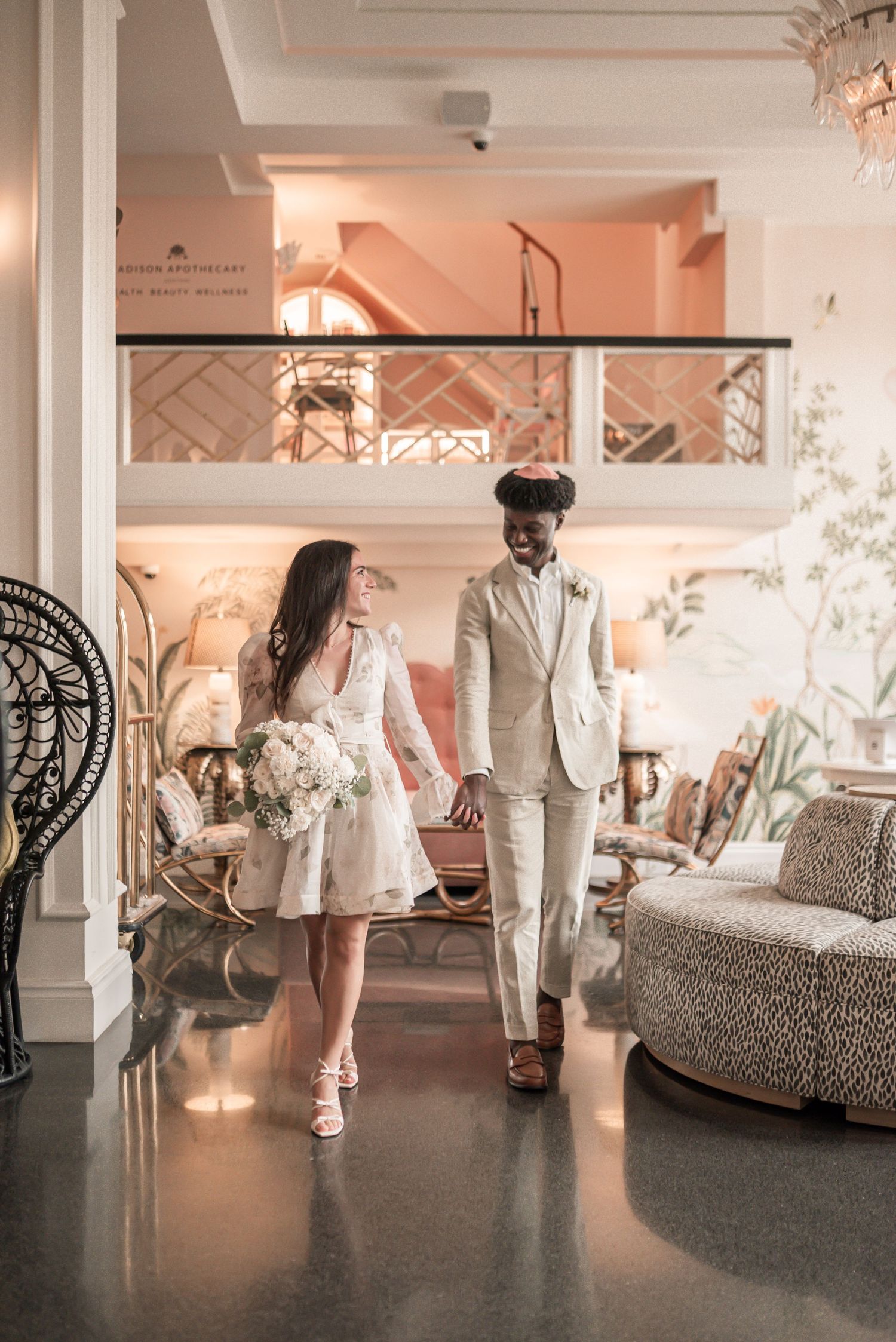 A couple in white attire dancing together in an elegant indoor venue with warm lighting and decorative pillars.