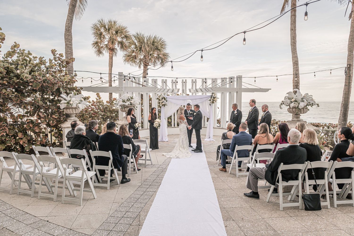 Multiple views of a beachside wedding venue setup with white chairs and palm trees under string lighting.