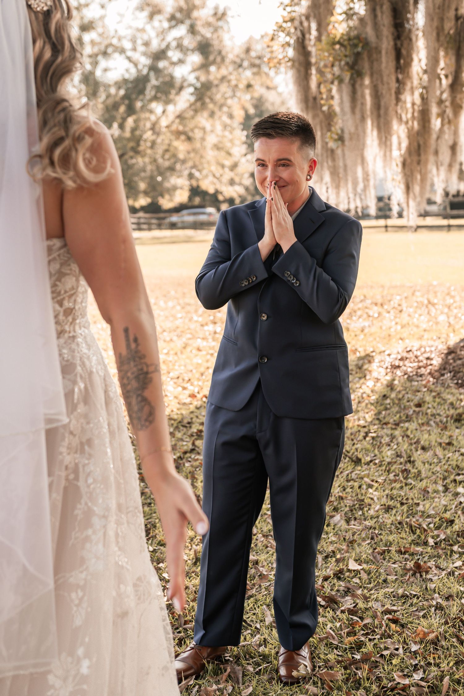 An emotional groom in a navy suit reacts during a first look wedding moment beneath moss-covered trees.