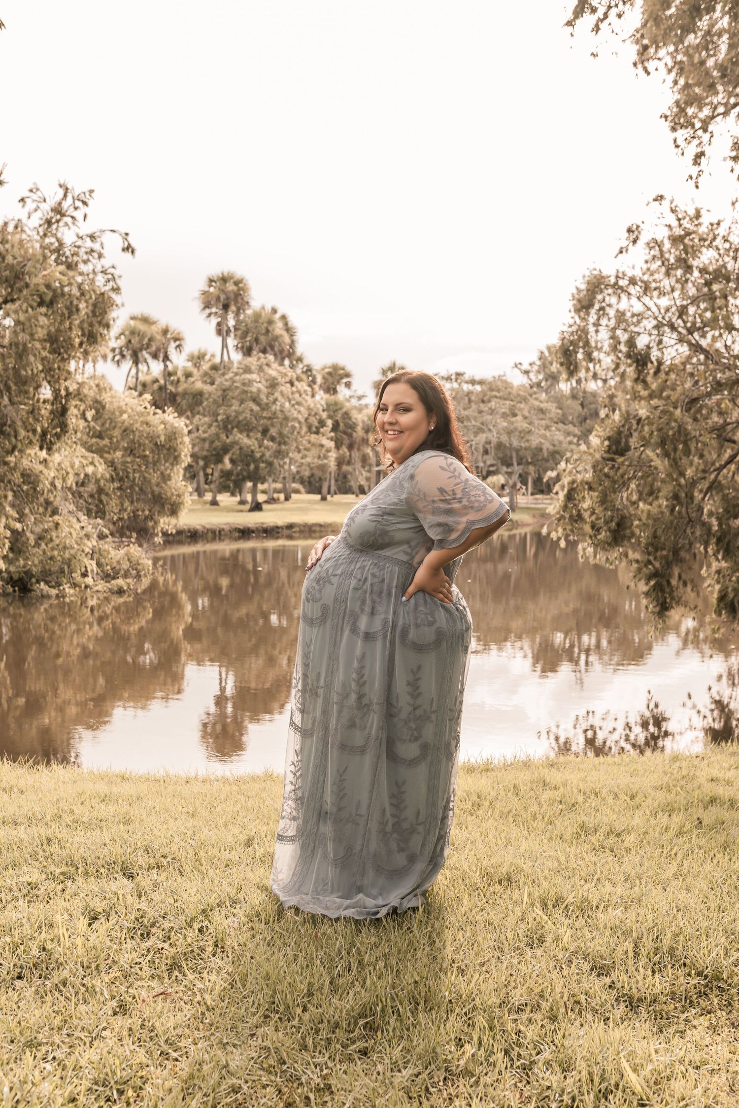 A figure wearing a billowing lace dress stands by a tranquil lake in a series of dreamy, sepia-toned photographs.