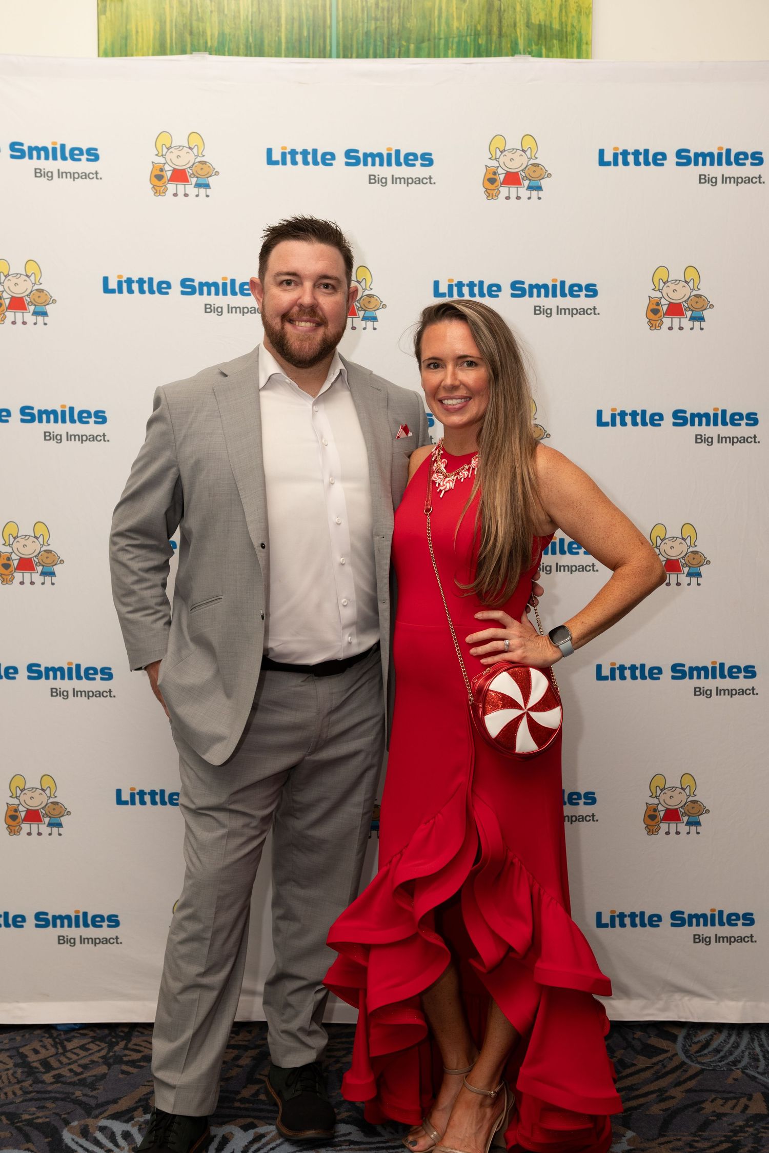 A couple poses together at a Little Smiles charity event, with the woman wearing a ruffled red dress.