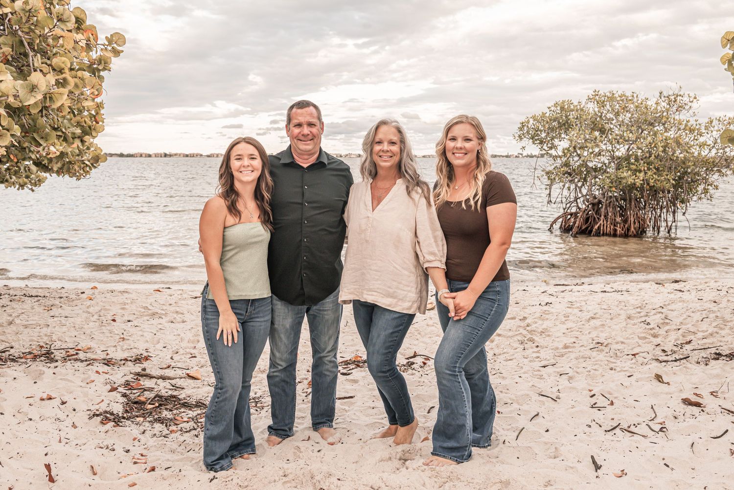 A group poses together on a sandy beach with mangroves and water in the background during sunset.