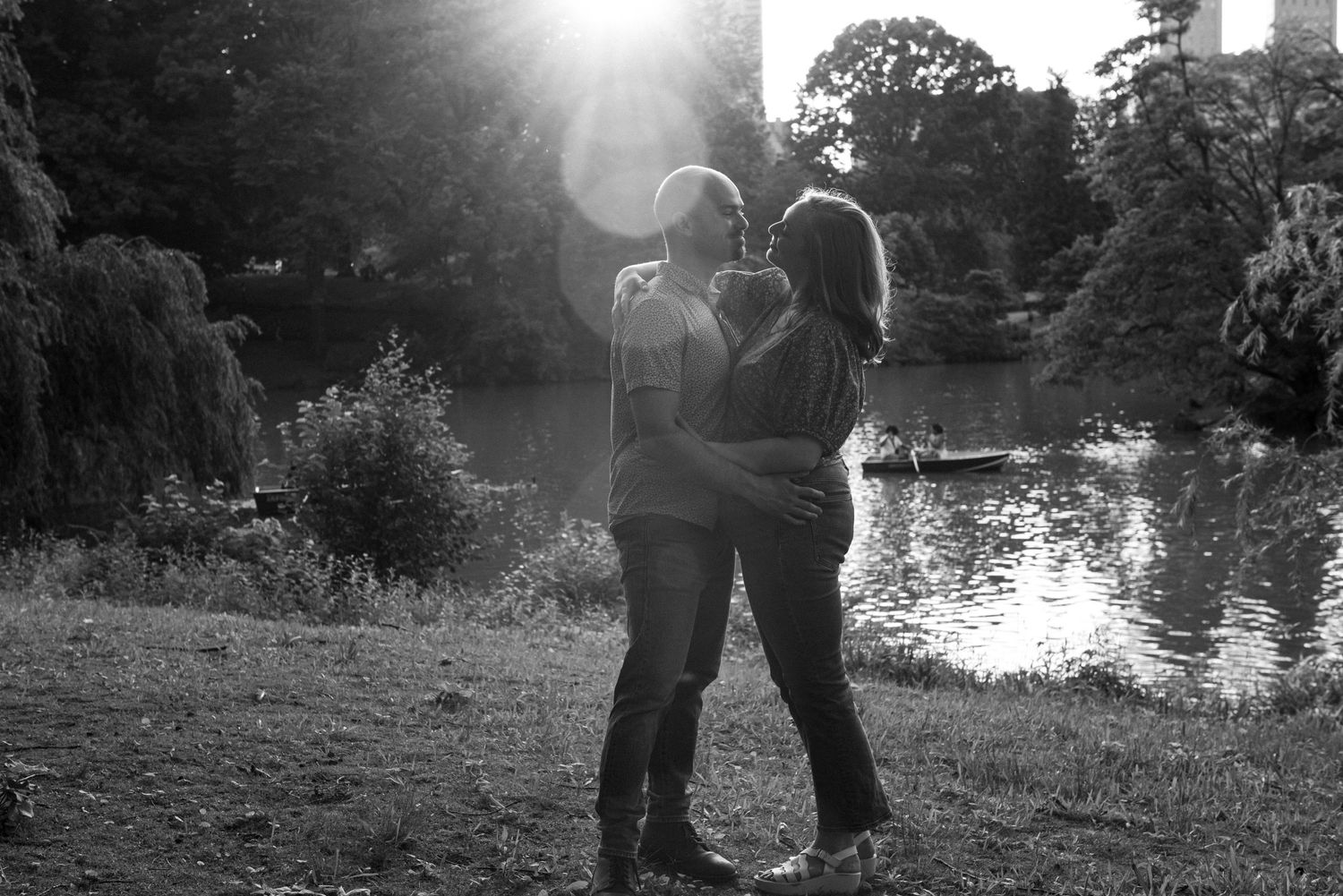 Silhouetted couple embraces by a lake at sunset in black and white nature scene.