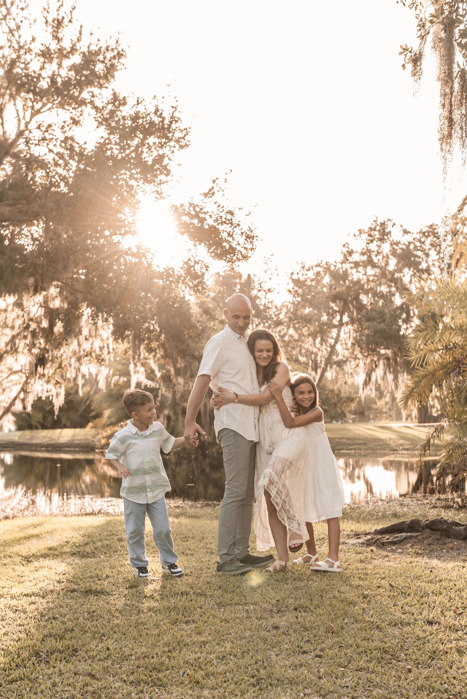 Family enjoying a golden sunset moment together by a tranquil lake with Spanish moss draped trees in the background.