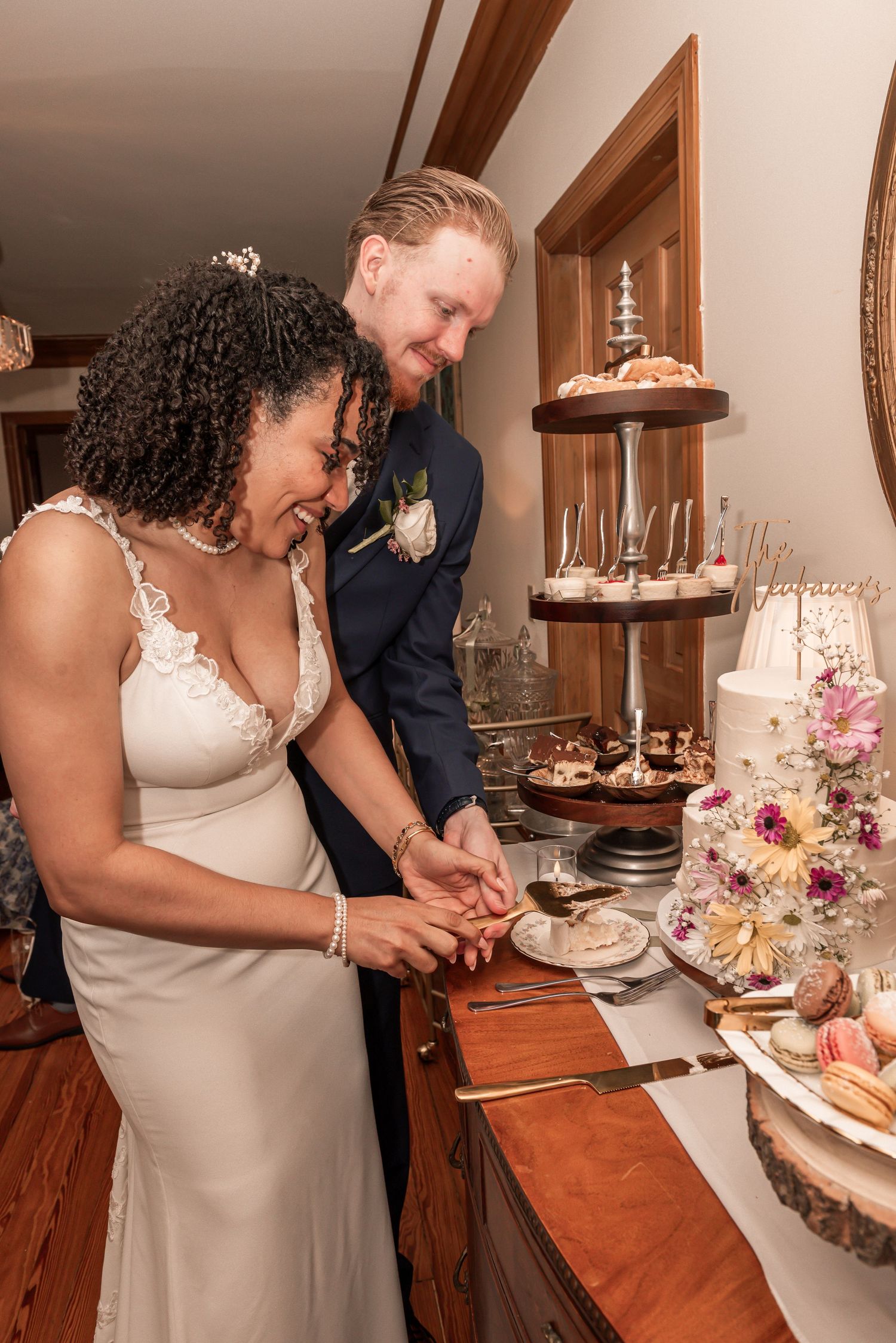 Bride and groom cutting their wedding cake together, smiling joyfully at an elegant indoor reception.