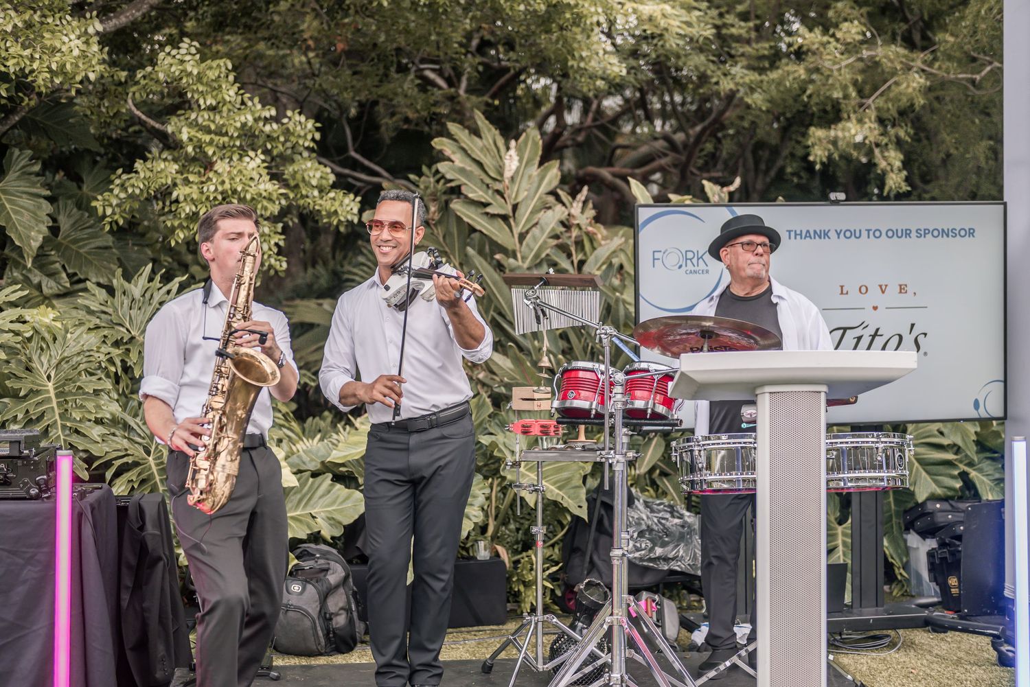 A jazz band performs outdoors with saxophones and other instruments on a sunny day in a park setting.