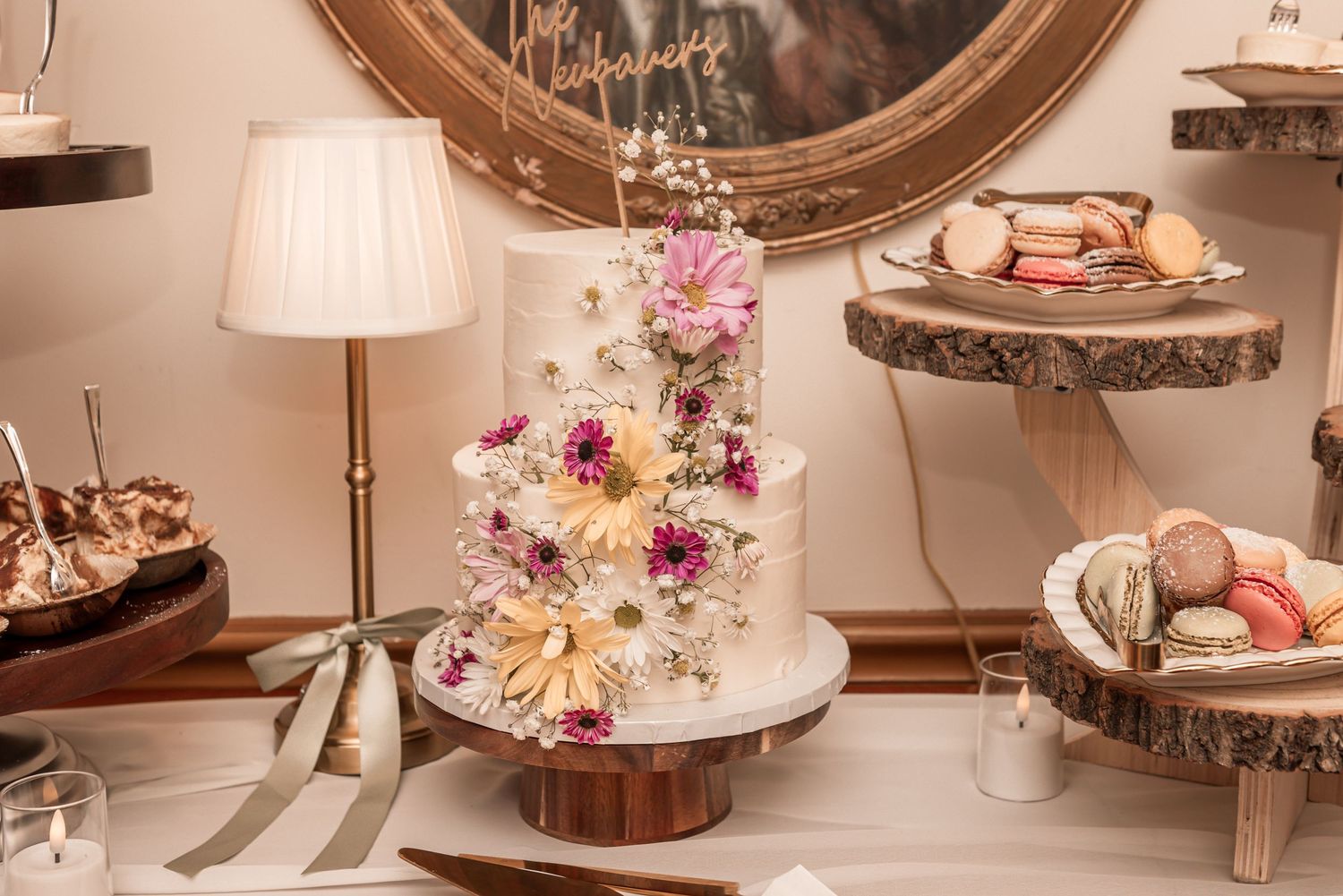 Elegant white wedding cake adorned with colorful dried flowers displayed on a rustic wooden cake stand.