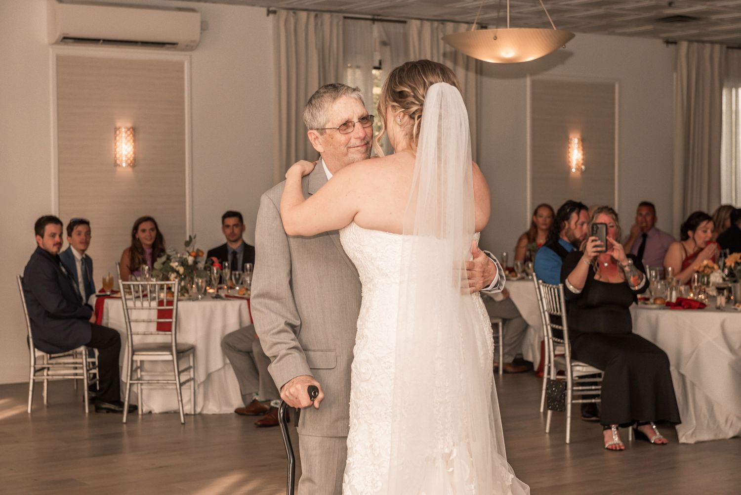 A wedding couple shares their first dance in a bright, modern industrial reception space with pendant lighting and white decor.