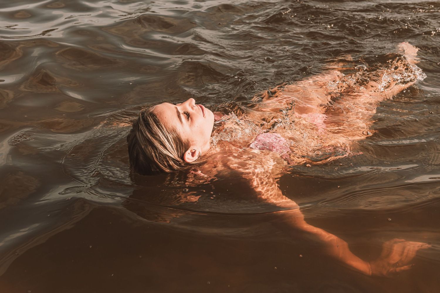 Woman floating on her back in dark water, hair spread out, enjoying a peaceful swim outdoors.