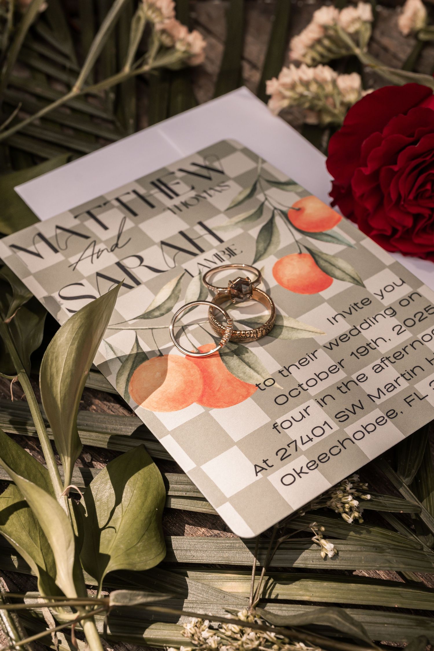 Wedding invitation with rings and red roses laid on a dark surface in artistic lighting.