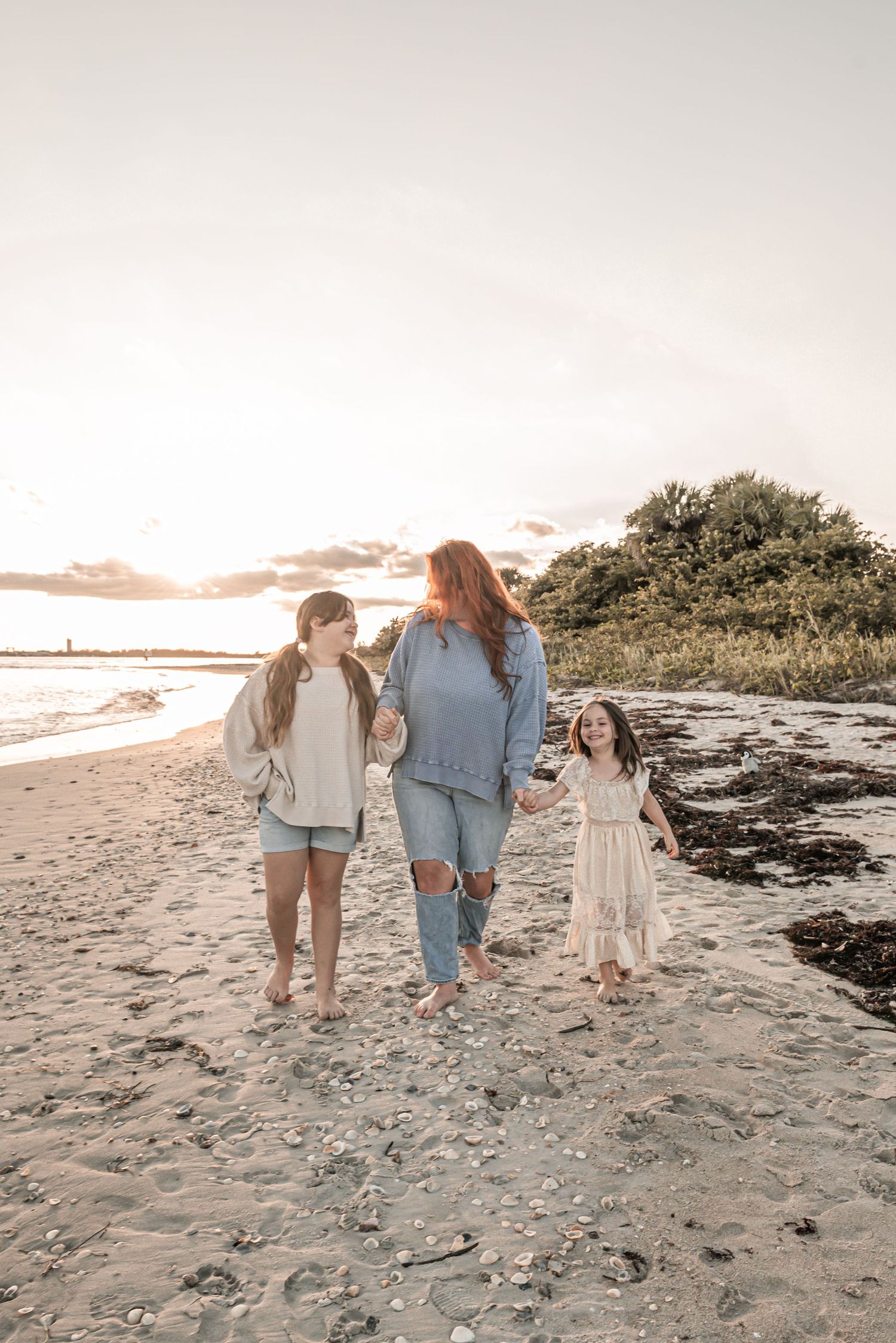 A family walks together along a scenic beach at sunset, creating silhouettes against the sand and sky.