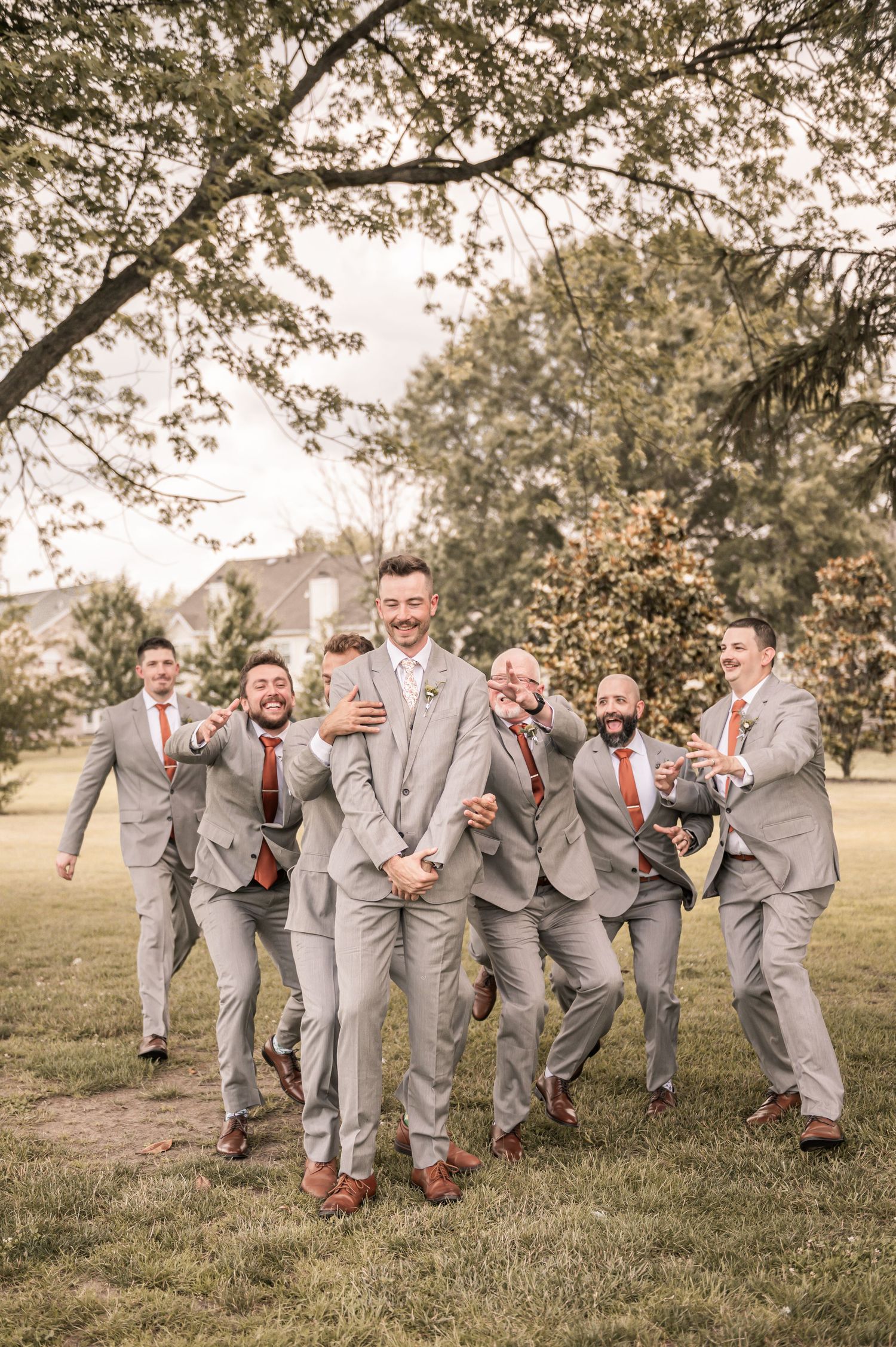 A wedding party in light gray suits and red ties playfully pose in a series of candid group shots on a grassy lawn.