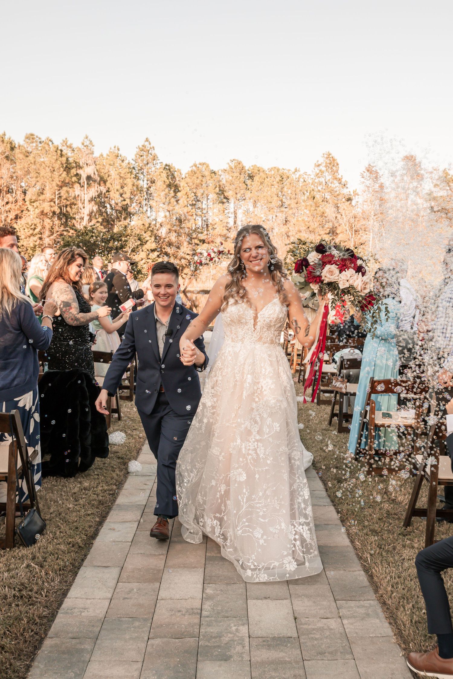 A wedding couple walks down an aisle while guests throw confetti during their joyous outdoor ceremony celebration.
