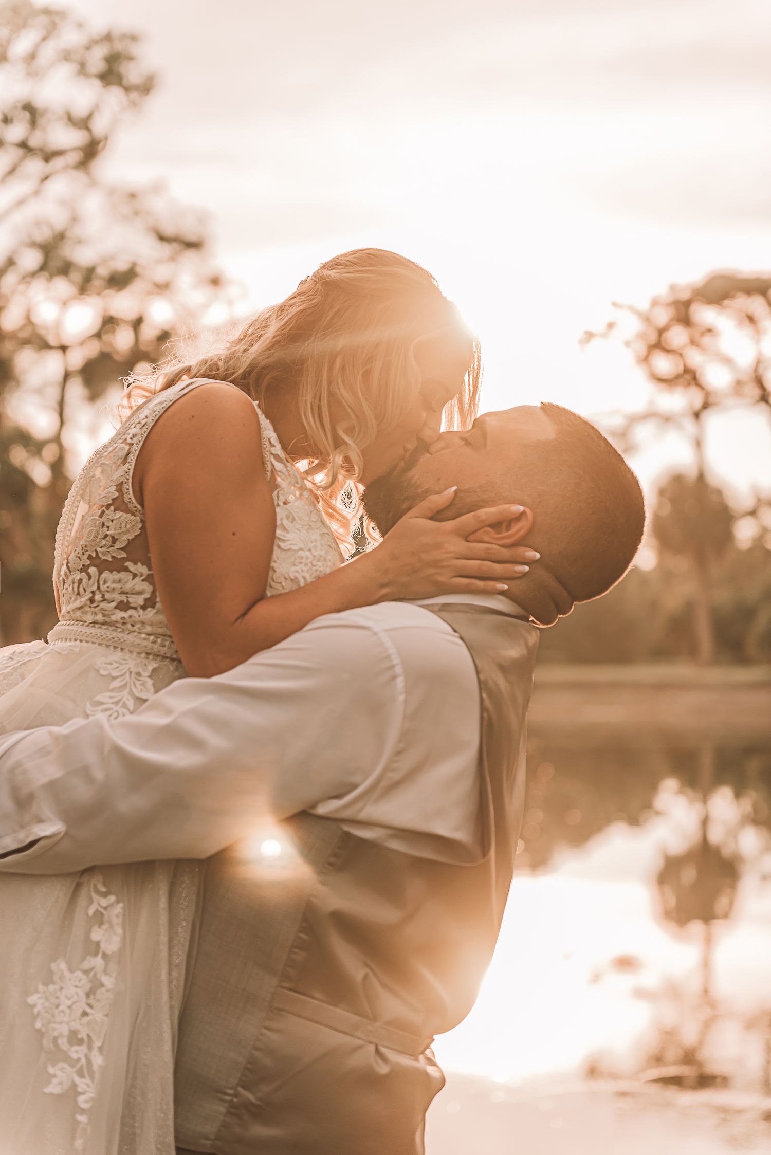 A romantic sunset wedding photo of a couple embracing by a reflective lake.