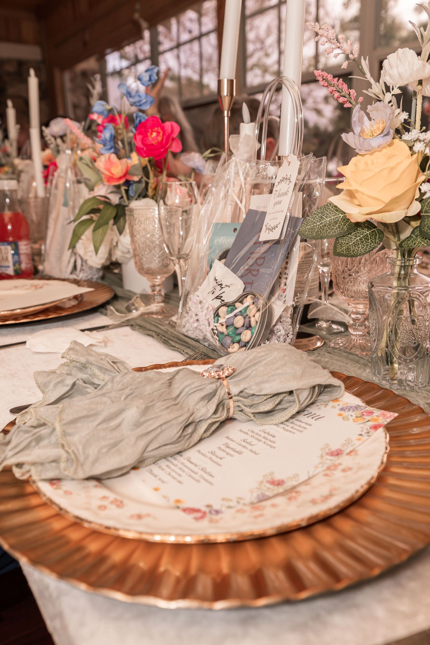 Elegant wedding reception table with floral china, sage napkins, and colorful flower centerpieces.