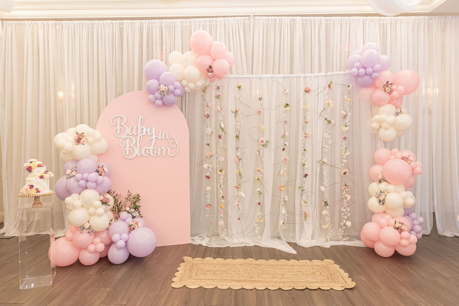 Pastel pink and purple balloon arch with teddy bear decorations against a white curtain backdrop for a baby shower event.
