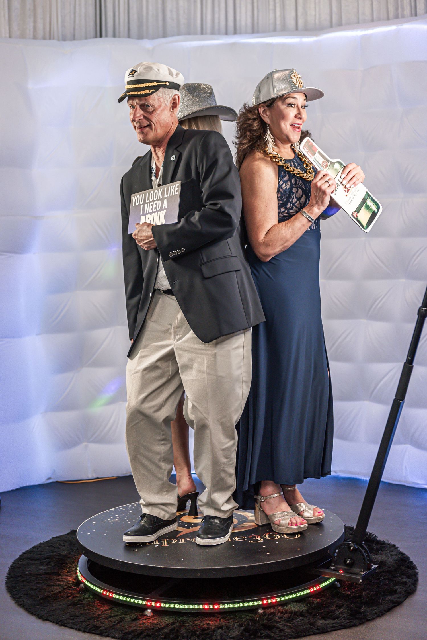 A couple in evening attire stand back-to-back on a circular rotating platform with lights around the edge.