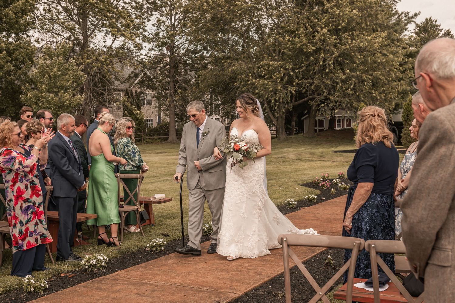 A wedding ceremony takes place outdoors with guests gathered around on a sunny autumn day in a park setting.