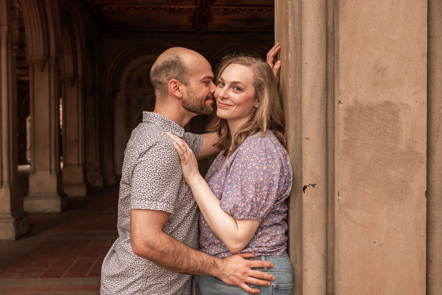 A romantic couple embraces in a covered hallway with arched columns while wearing coordinating floral print outfits.