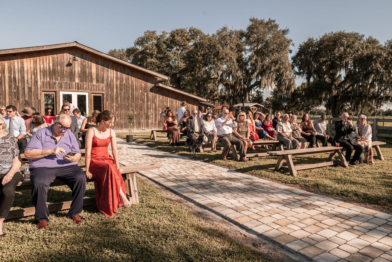Rustic barn wedding venue surrounded by trees with guests gathering for an outdoor celebration.