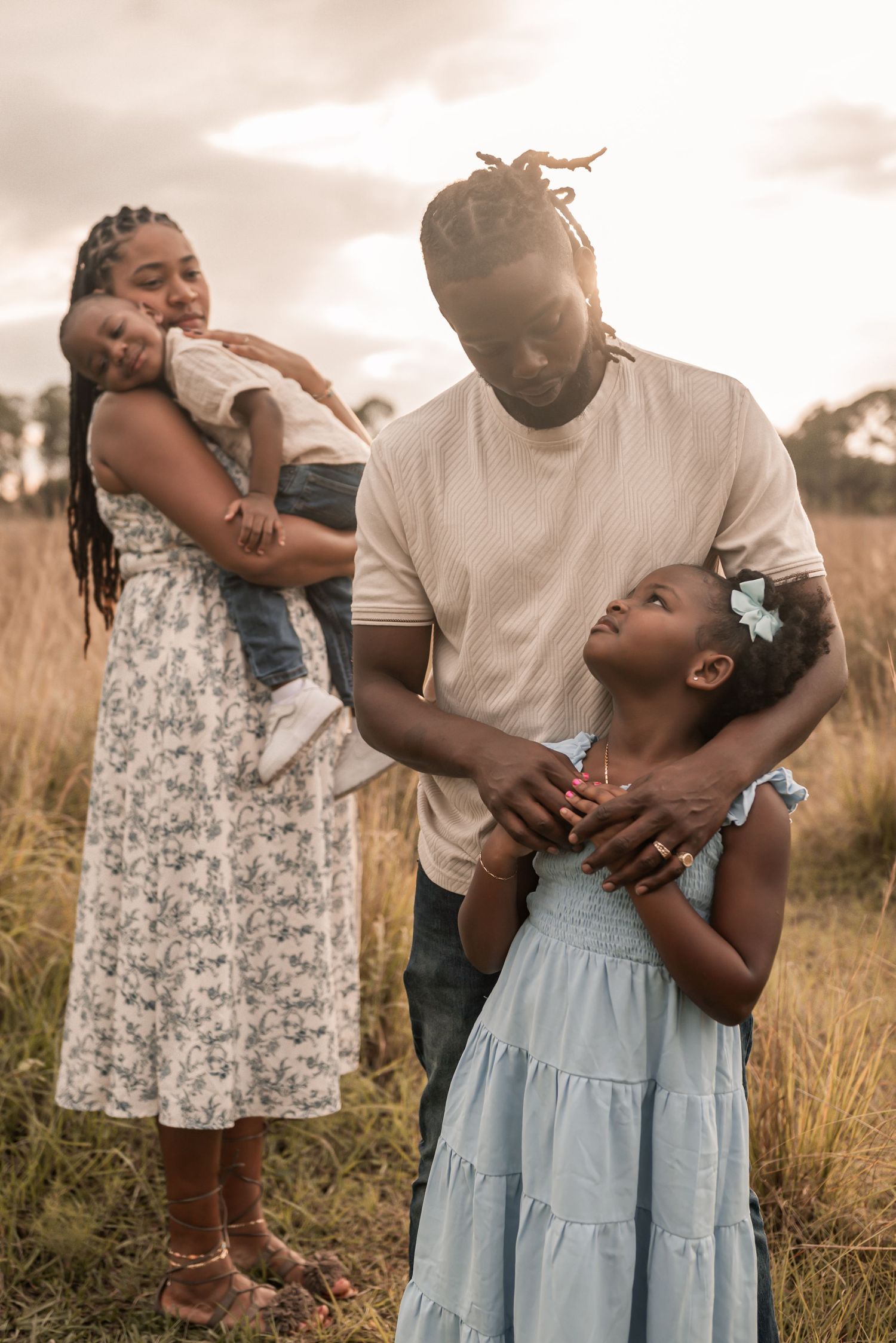 A loving family embraces and shares joyful moments together in a sun-lit field with tall grass.