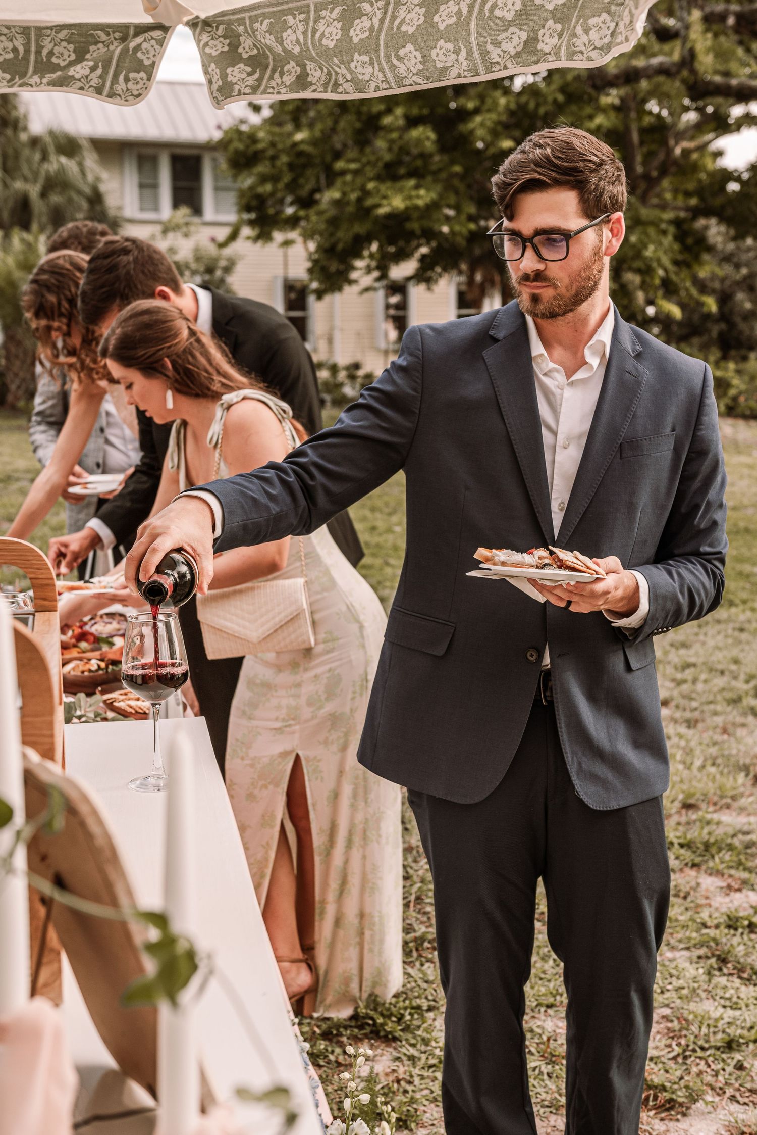 Wedding guests in formal attire pour champagne and toast during an outdoor celebration.