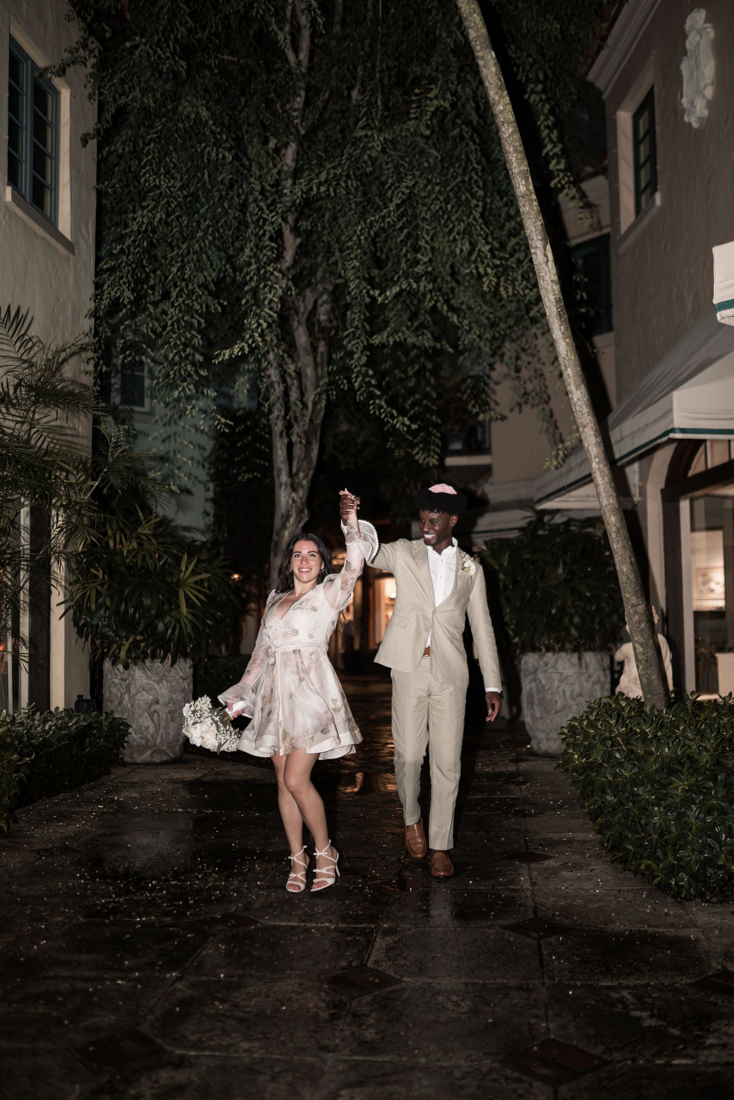 A couple walks together at night along a tree-lined path with dramatic lighting and shadows.