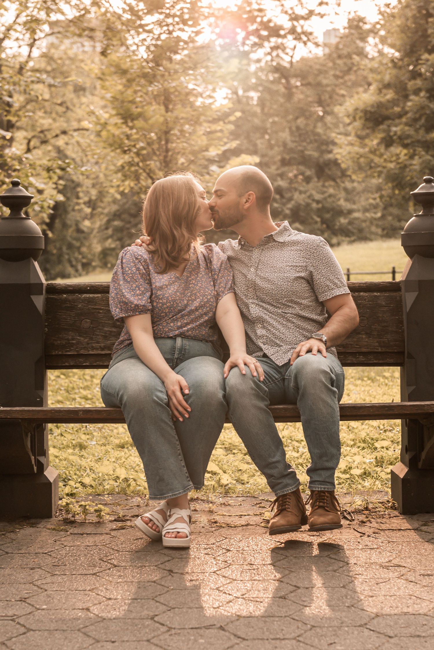 A couple sits close together on a wooden bench in a park setting with warm autumn tones in the background.