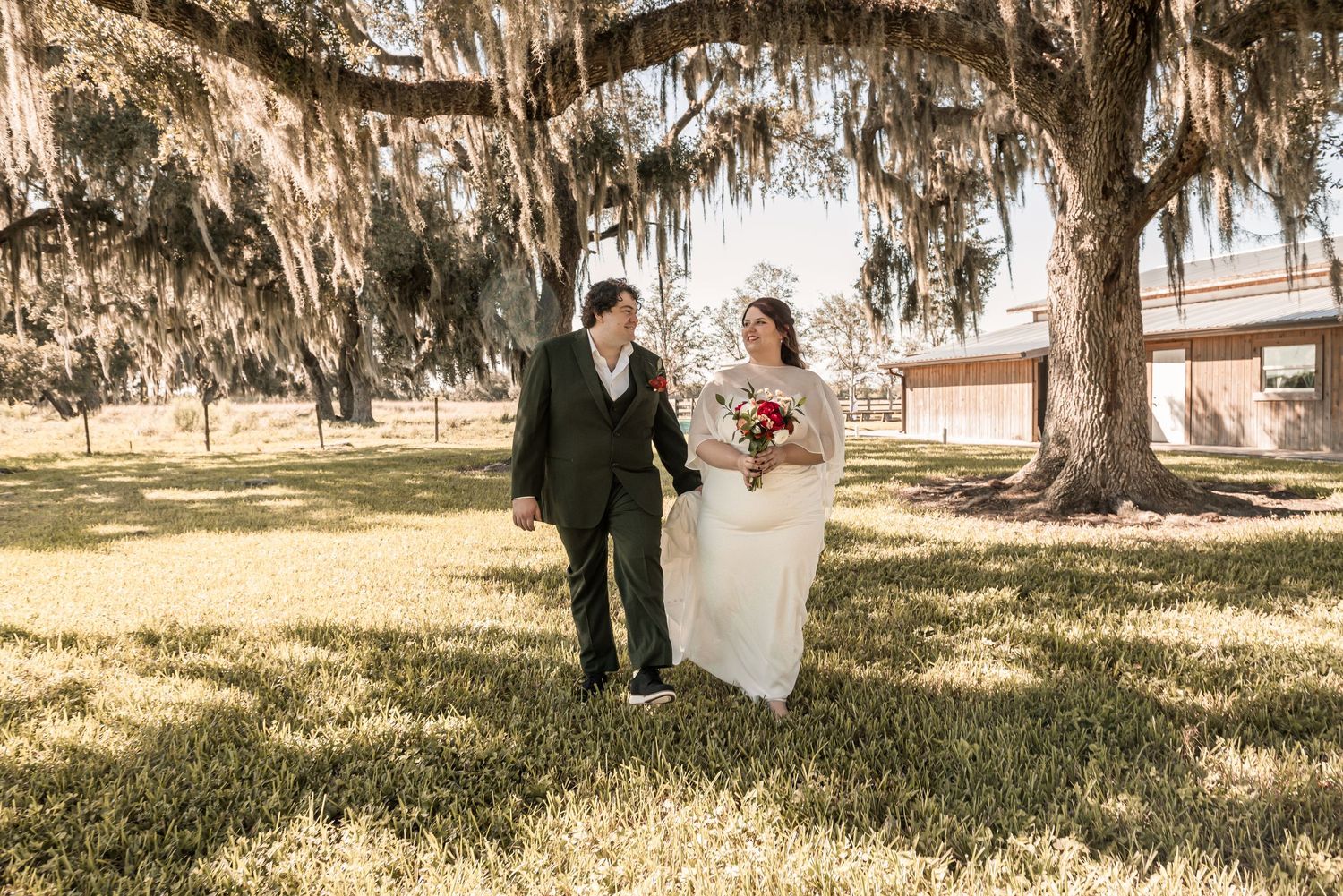 Wedding ceremony taking place under majestic oak trees draped with Spanish moss on a sunny afternoon.