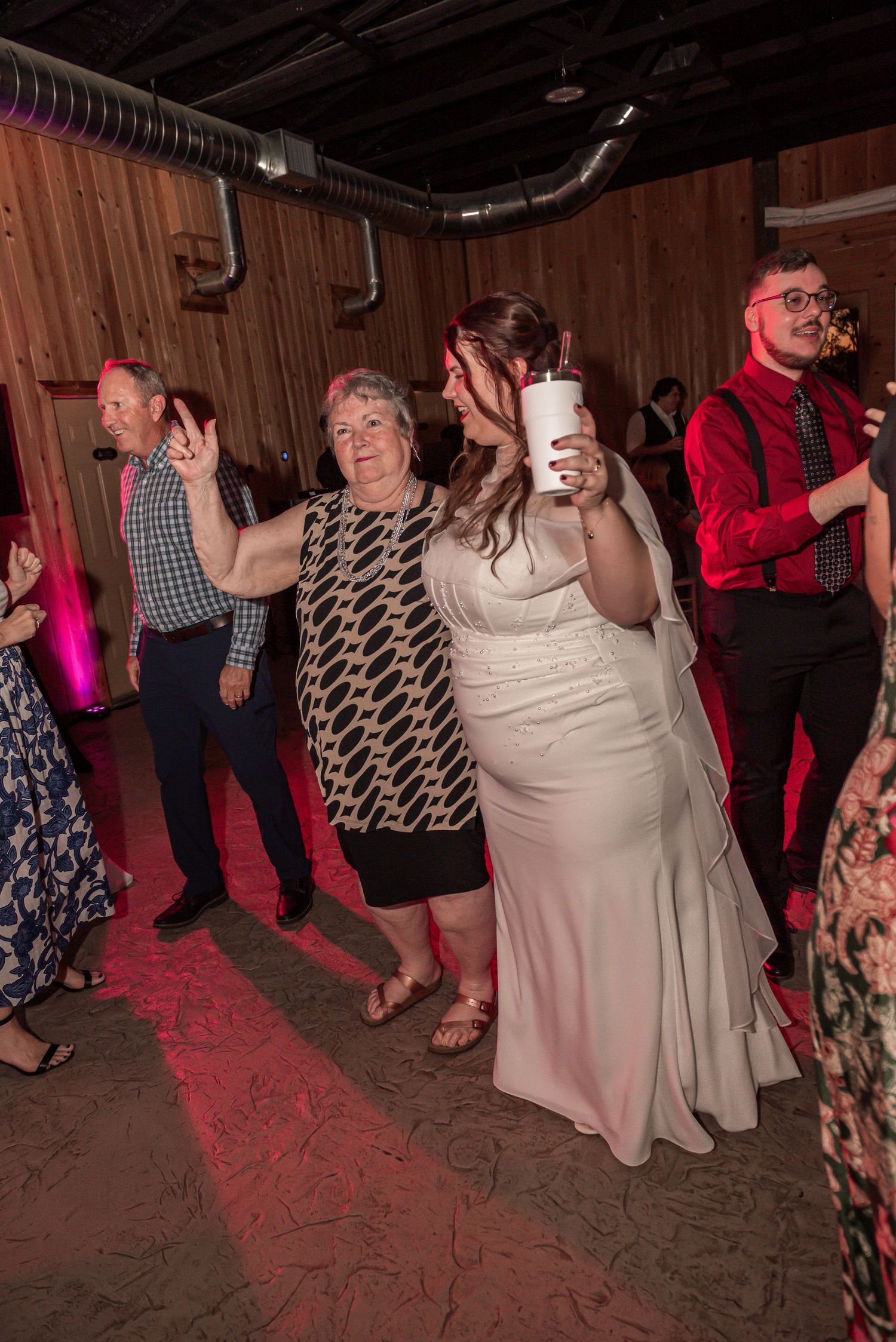 People dancing together at a rustic venue with pink lighting and wooden walls during a lively celebration.