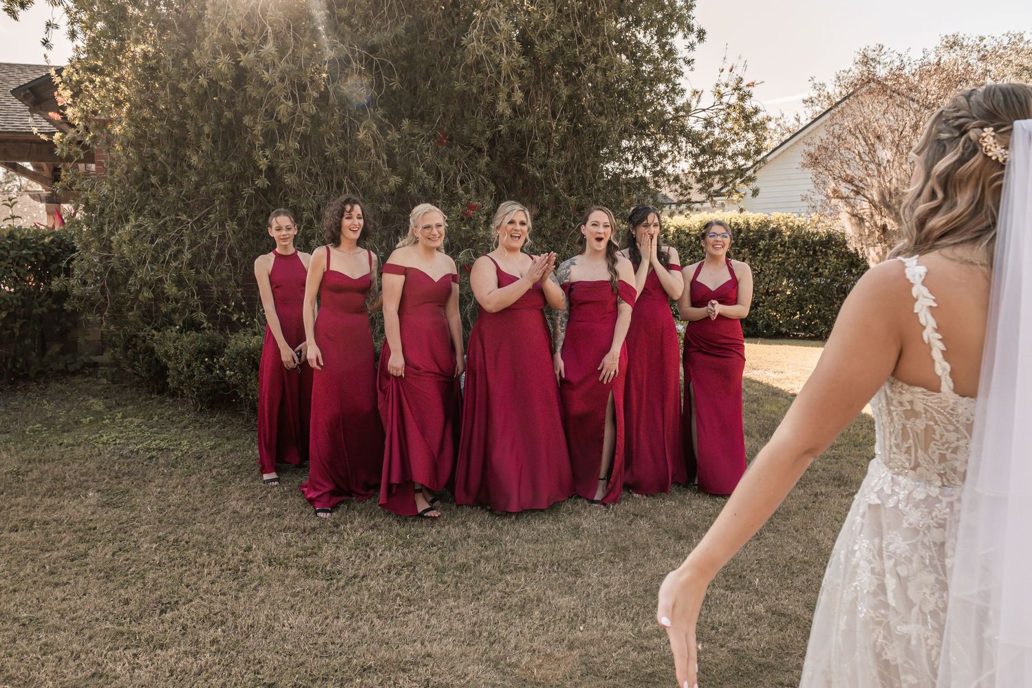 A wedding party in burgundy dresses poses together outdoors during a fall ceremony.