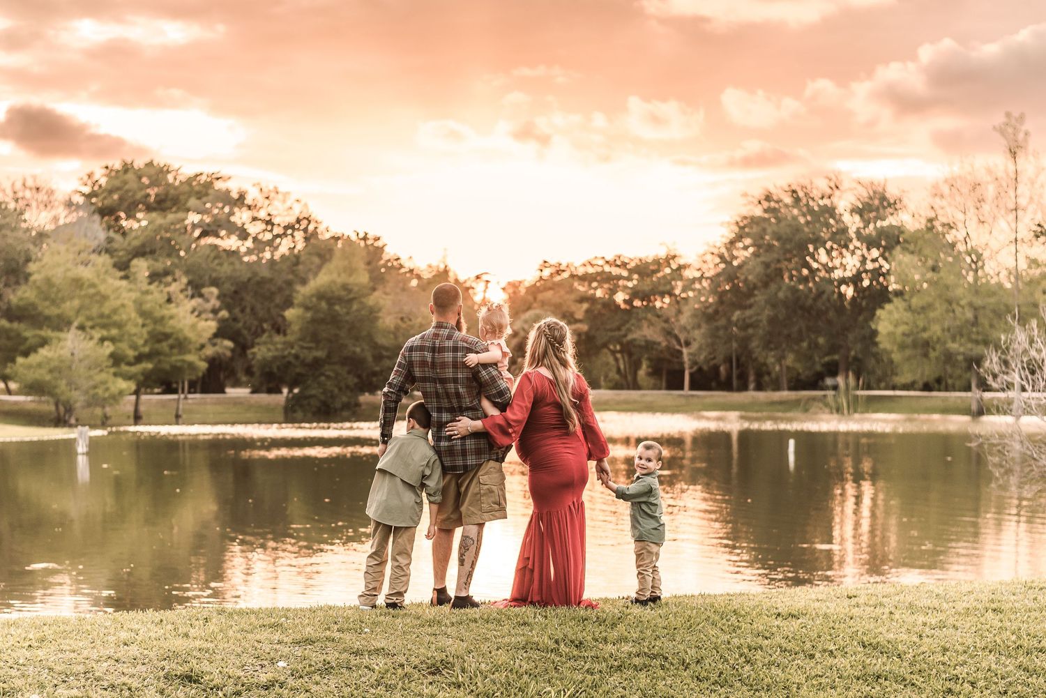 A family stands together at sunset by a serene lake, silhouetted against warm pink skies and reflected waters.