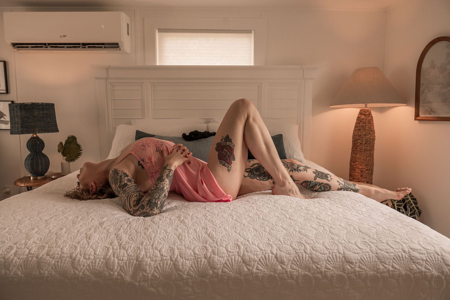 A sleeping figure reclines on a white bed with warm lighting from a bedside lamp in a cozy bedroom setting.