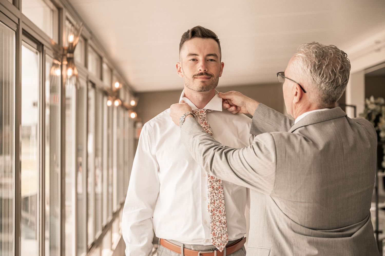 Man in formal attire preparing for wedding celebrations in a bright hallway setting.
