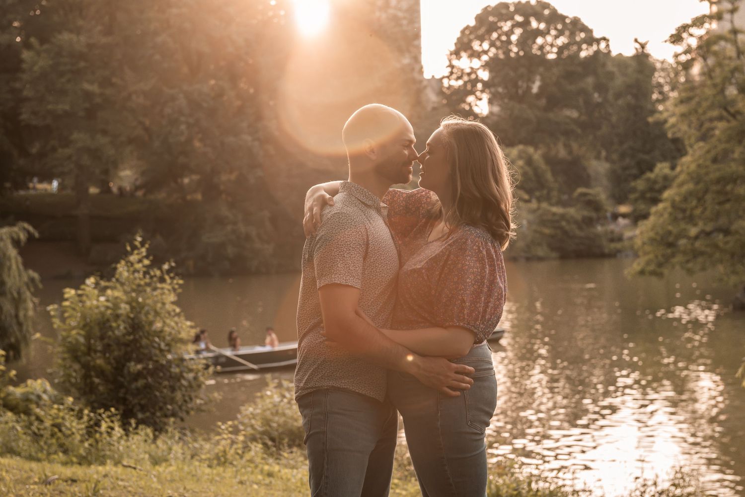 A couple shares an intimate moment by a tranquil lake during golden hour as sunlight filters through trees.