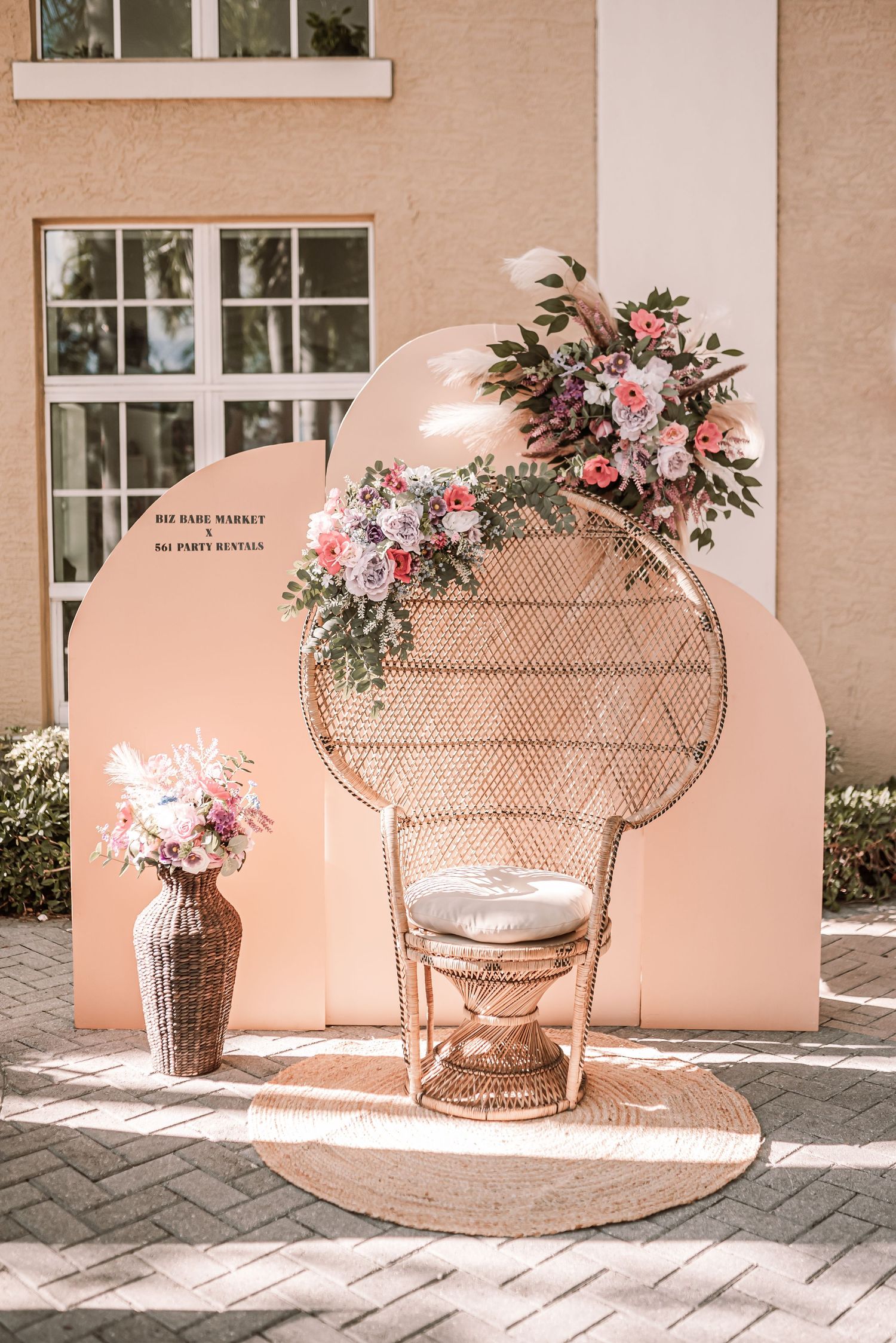 Bohemian wedding setup with a peacock chair, arch backdrop, and floral arrangements in soft pink and blush tones.