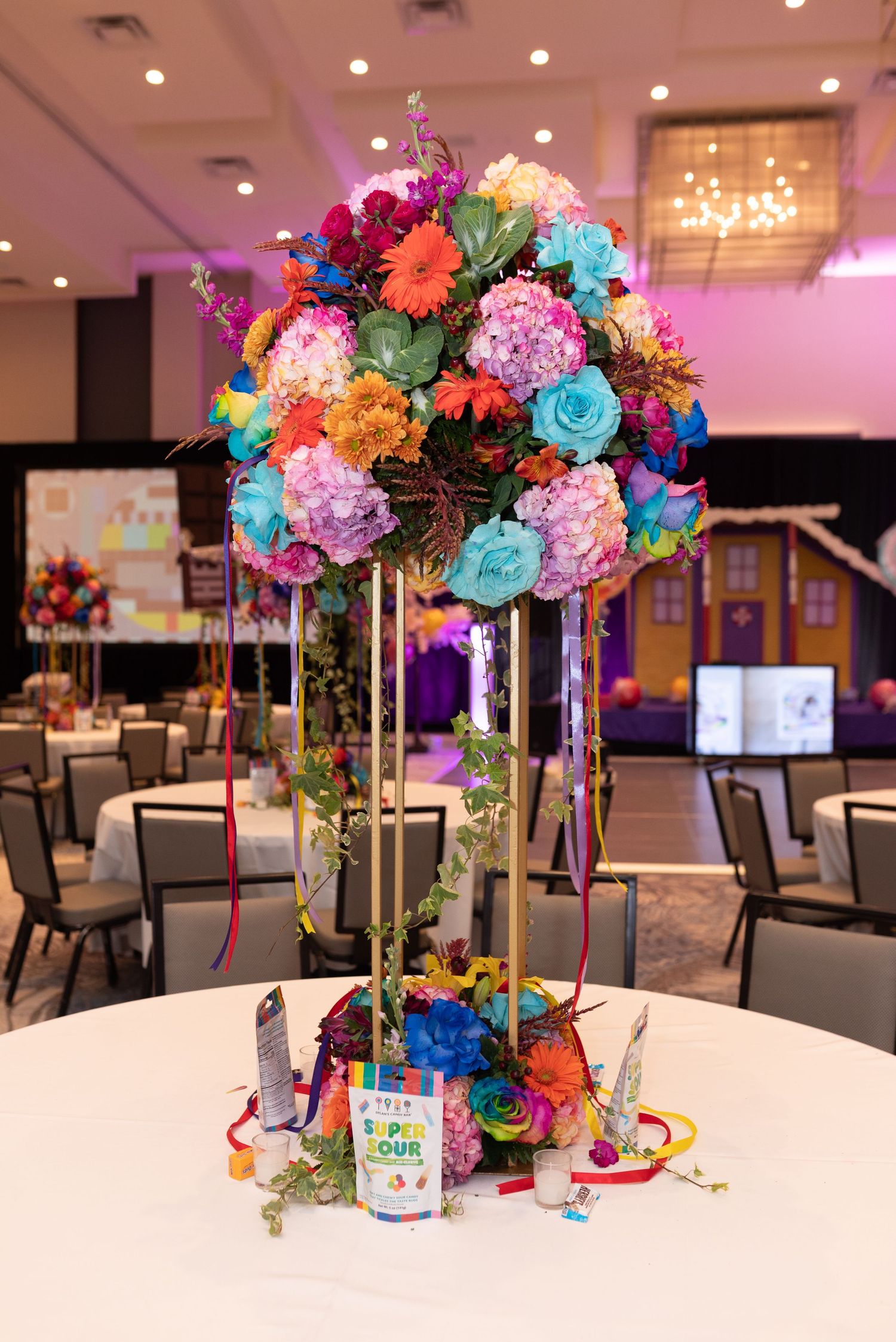 Colorful floral centerpieces with vibrant roses and hydrangeas decorate tables at an elegant indoor event venue.