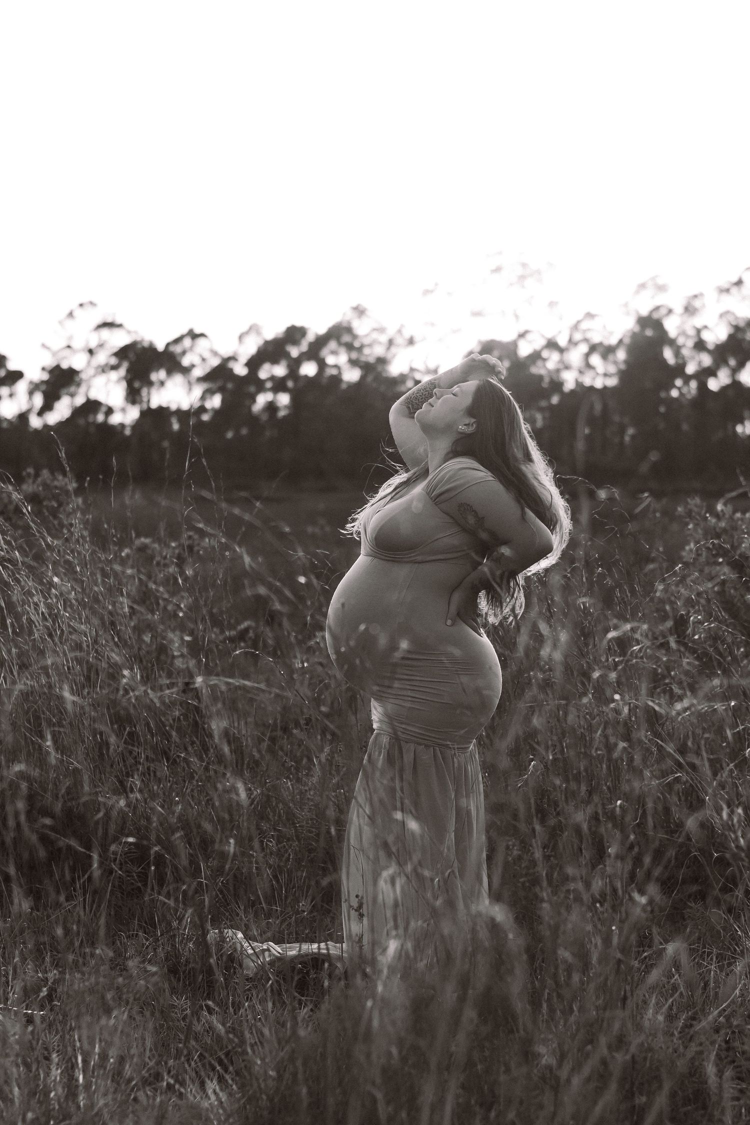 A silhouetted maternity portrait of an expecting mother in a field at dusk.