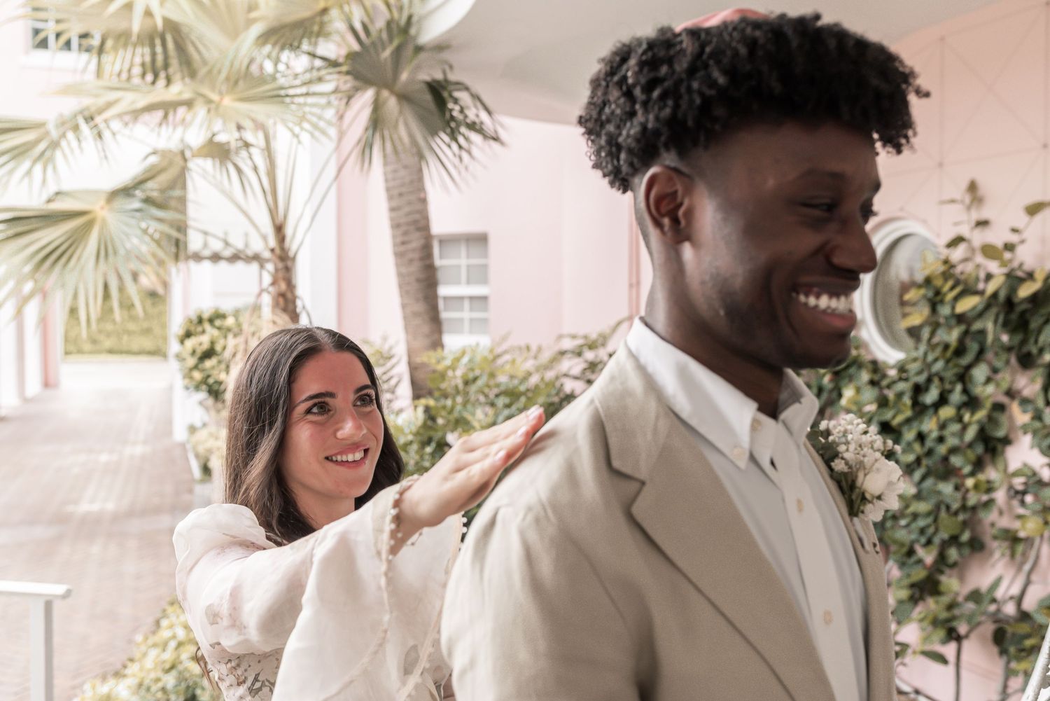 A joyful couple shares laughter during their outdoor wedding celebration surrounded by greenery and natural light.