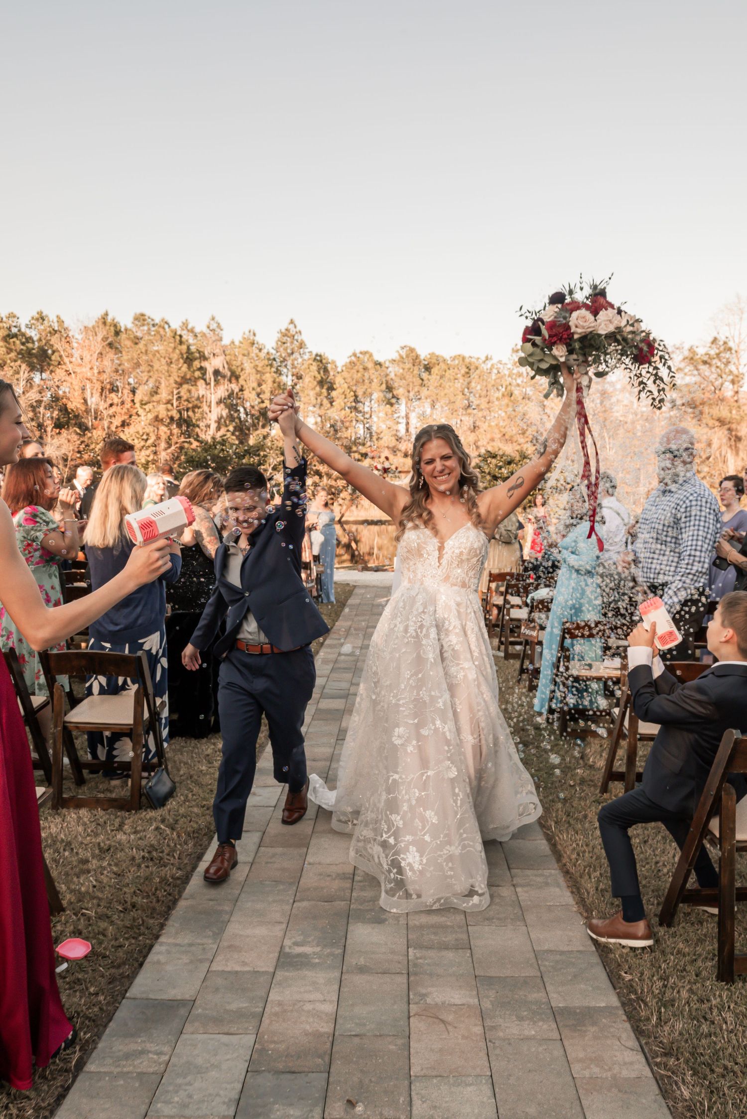 Wedding guests toss confetti over newlyweds walking down an outdoor stone pathway during golden hour celebration.