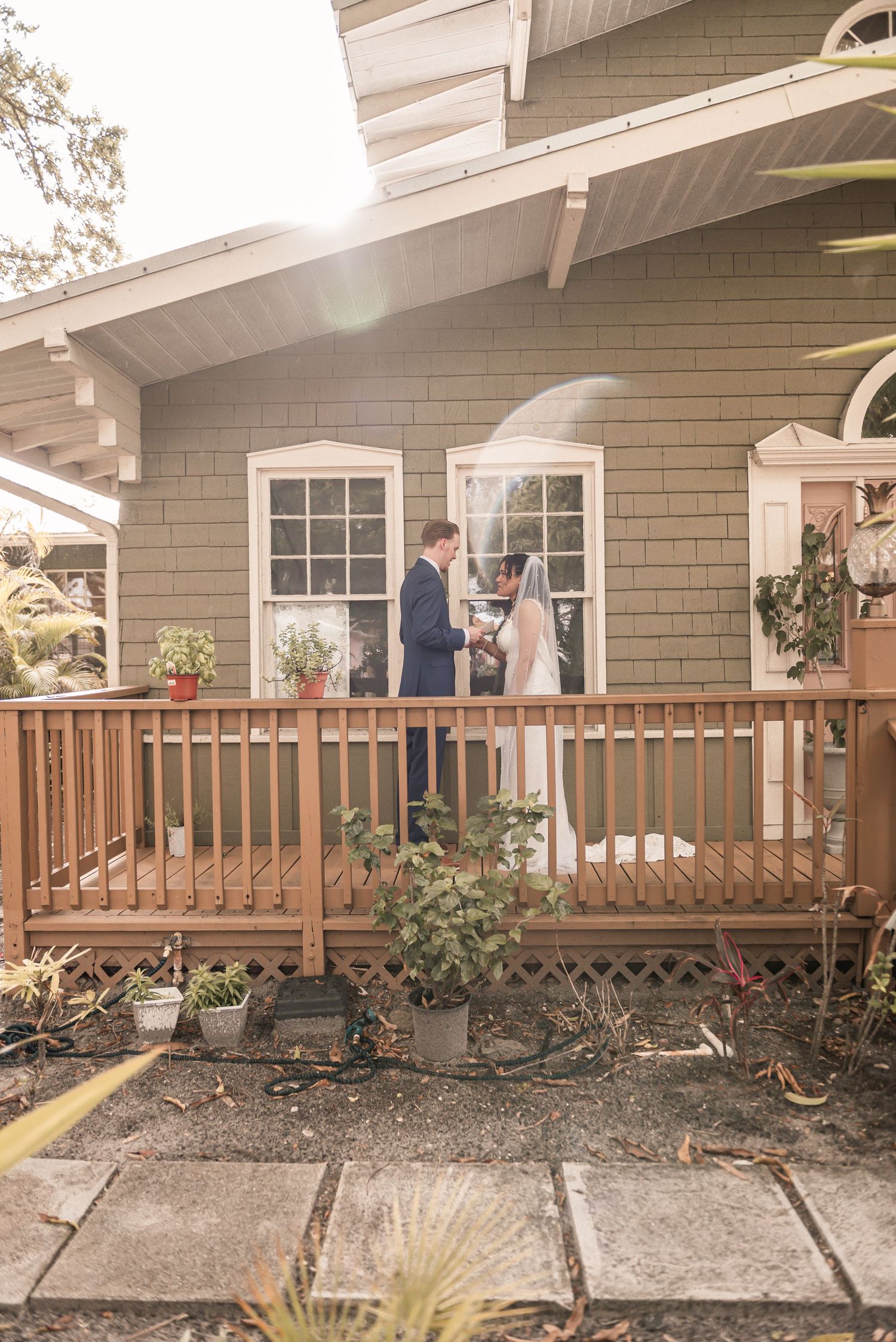 Bride and groom share first look moment on wooden porch of charming green cottage.