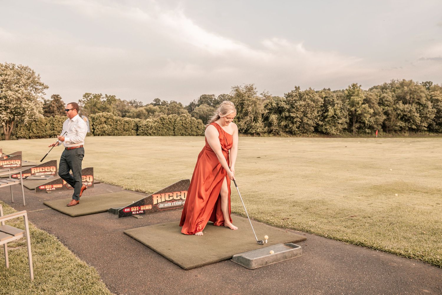 People practicing golf at a driving range with putting green and golf clubs on a sunny afternoon.