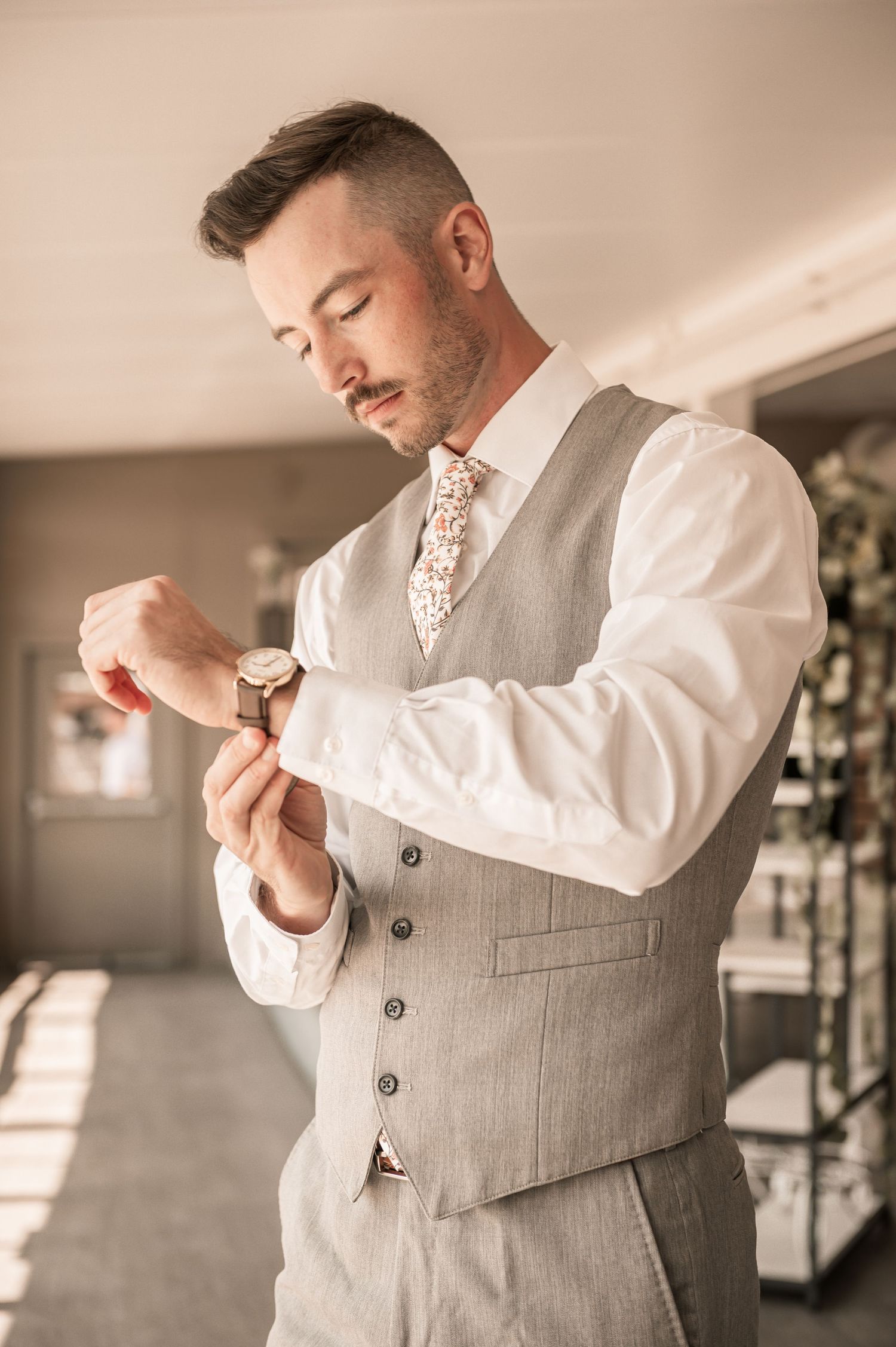 Groom in grey vest and white shirt adjusts his tie while getting ready for the ceremony.